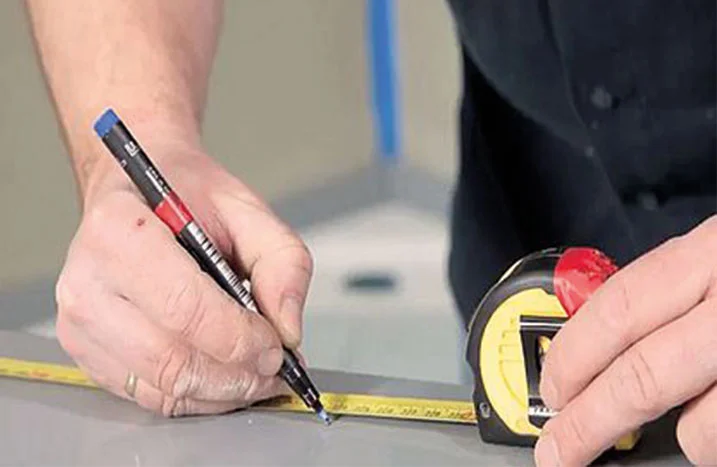 Person misst mit Zollstock und markiert mit Stift